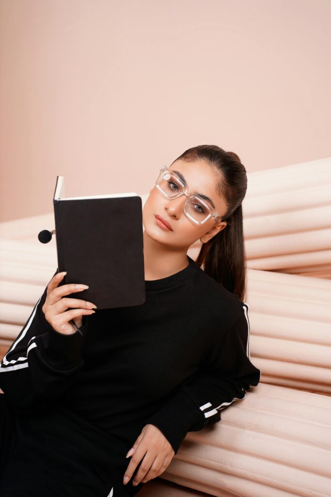 A young woman in sportswear and eyeglasses reads a book indoors, exuding focus and style.
