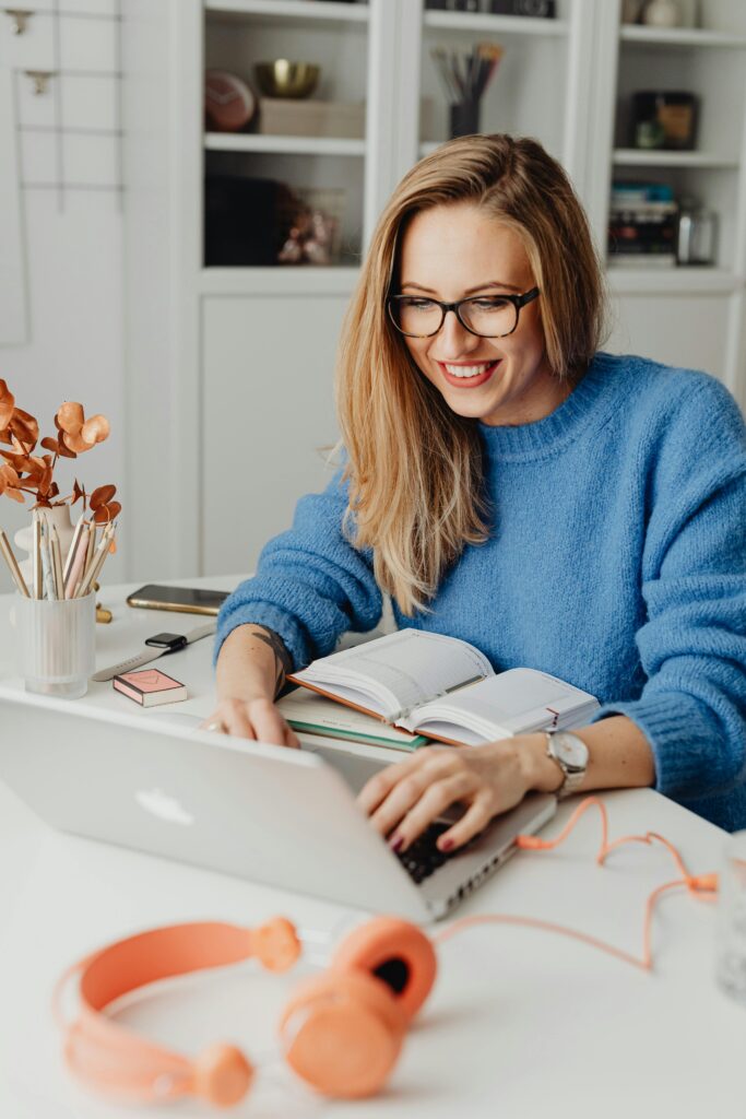 A cheerful woman in a blue sweater working remotely with a laptop in a cozy home setting.